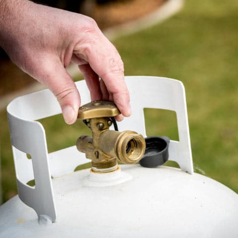 Man tightening the valve on a white propane tank
