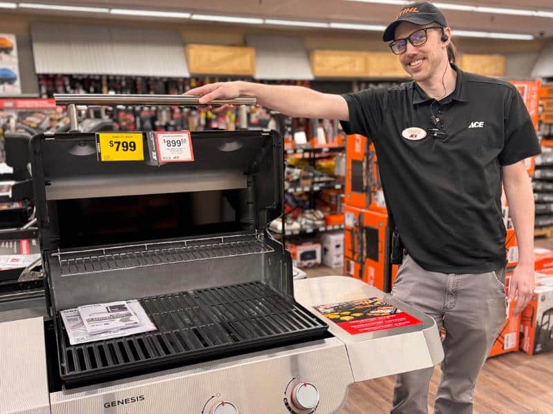 Ace Hardware employee showcasing a Genesis gas grill inside store with pricing signage visible