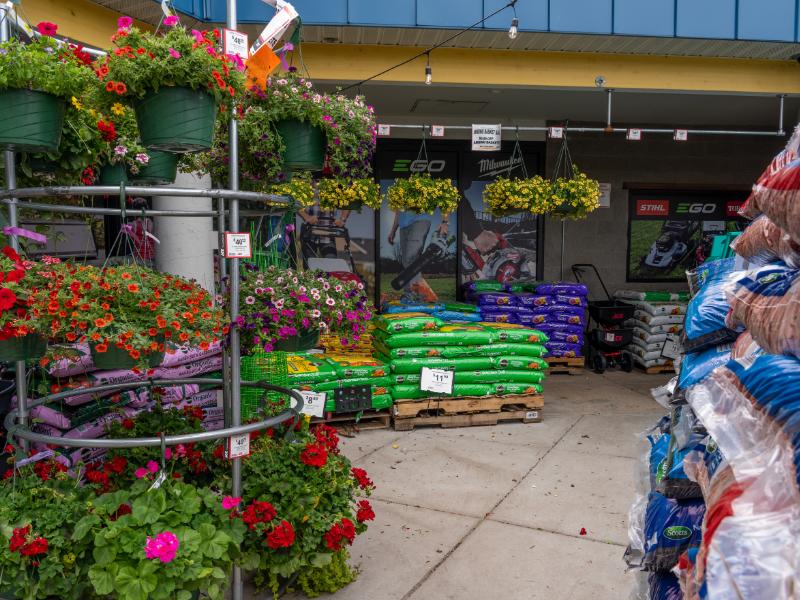 Colorful hanging flower baskets and garden soil bags displayed outside hardware store entrance