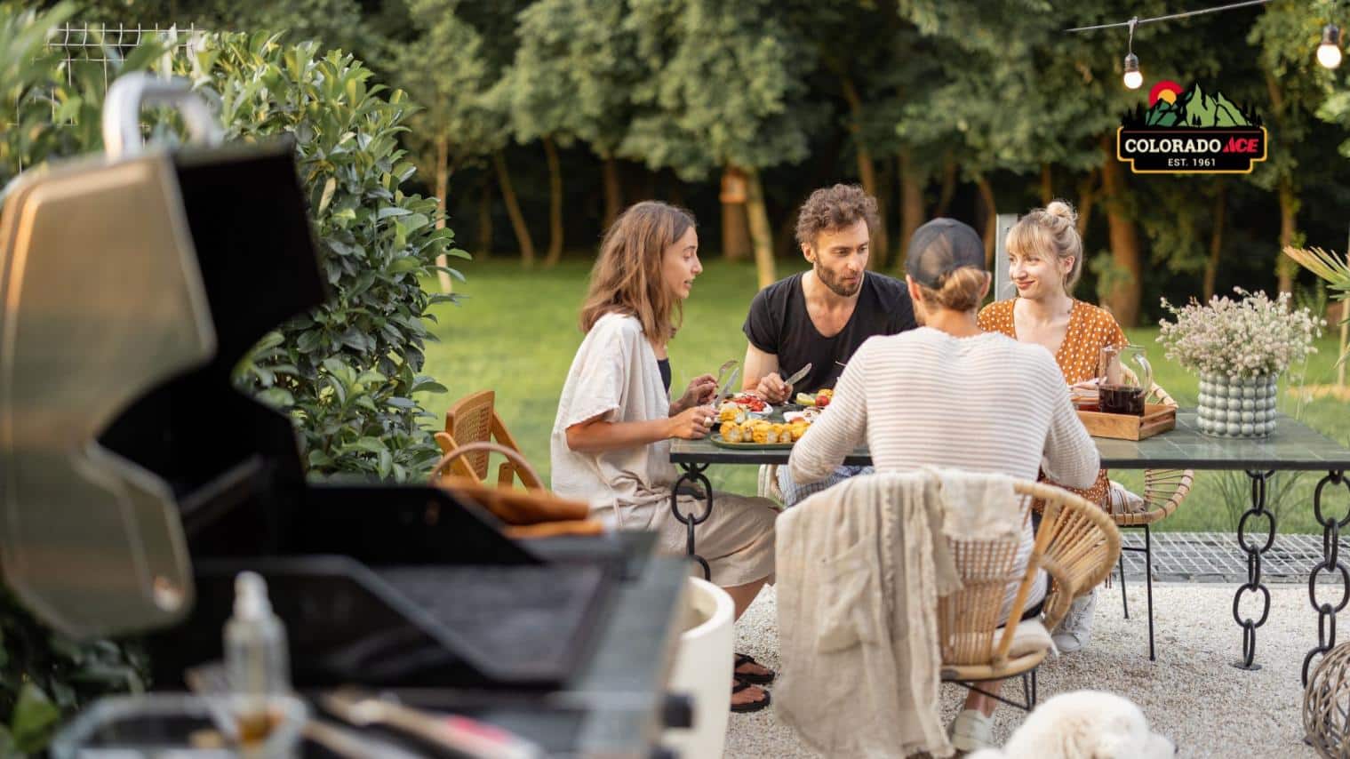 Friends enjoying a backyard barbecue and outdoor meal near a grill on a summer evening.