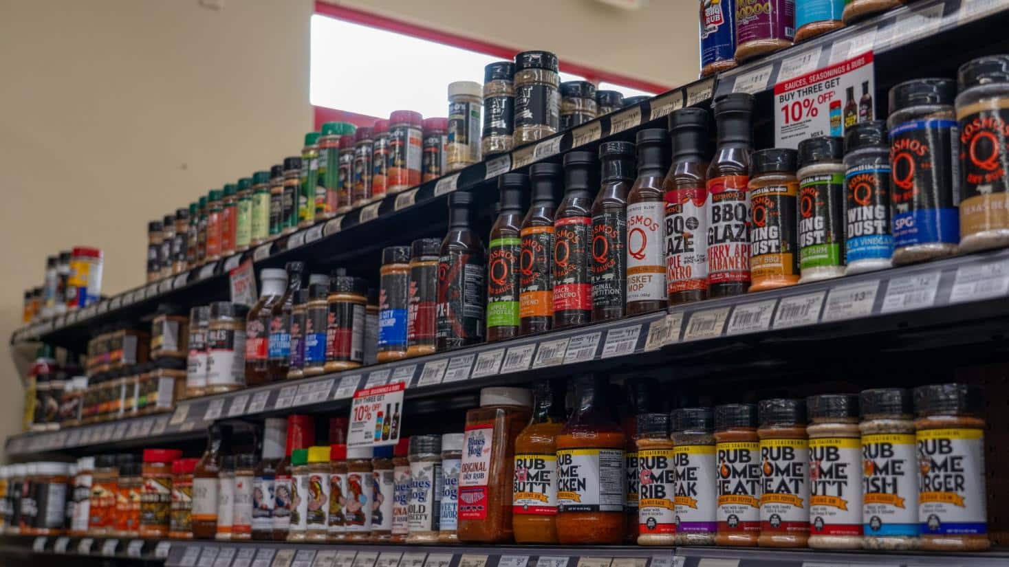 BBQ sauces, seasonings, rubs, and grilling essentials displayed on store shelves.v