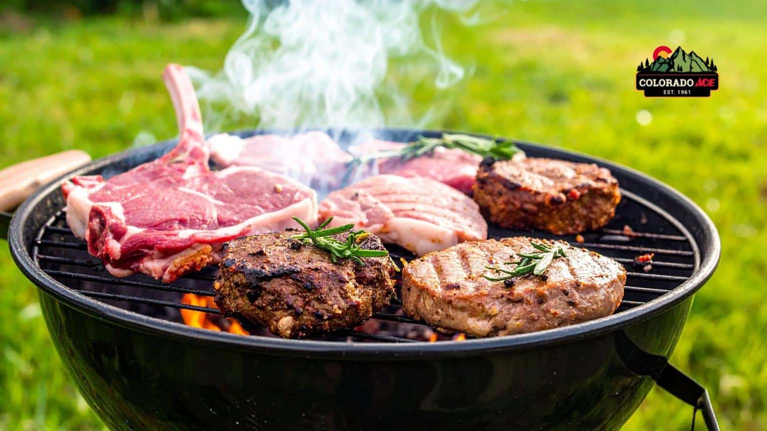 Steaks, burgers, and pork chops cooking on a charcoal grill outdoors.